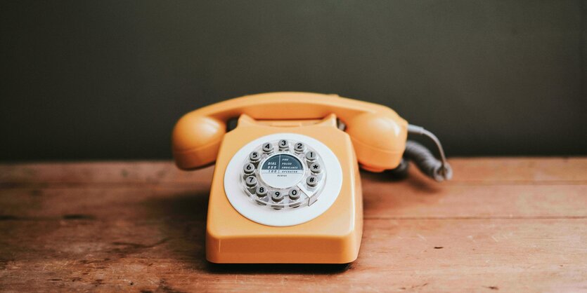 Ein orangenes Telefon mit Wählscheibe steht auf einem Holzboard