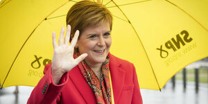 Nicola Sturgeon grüßt unter gelbem Sonnenschirm