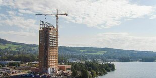 Ein Hochhaus aus Holz steht an einem See, daneben ein Kran