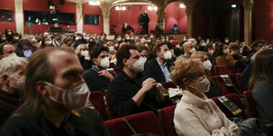 Menschen sitzen mit Maske in einem Theater