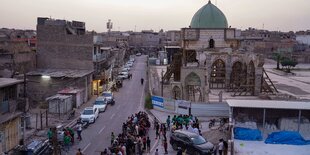 Ansicht eines Stadtteils von Mossul, mit Moschee und eine Gruppe Menschen um einen Tisch im Freien