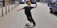 Ein Junge spielt Fussball auf der Straße