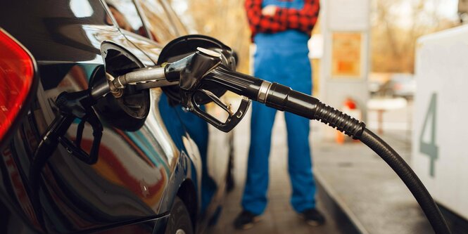 Ein Mann an einer Tankstelle ist hinter einem Zapfhahn zu sehen, der im Tank eines PKWs steckt