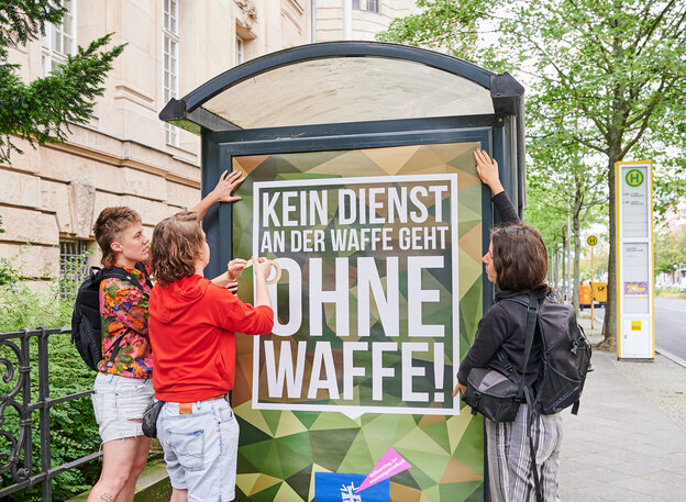 Aktivist*innen bringen ein Plakat der Bundeswehr mit abgeändertem Slogan vor dem Kriminalgericht in Moabit an.