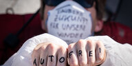 Auf den Fingern eines Aktivisten im Maleranzug steht "Autofrei"