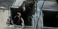 Ein Mann blickt aus einem Fenster, dessen Rahmen schwer beschädigt ist.