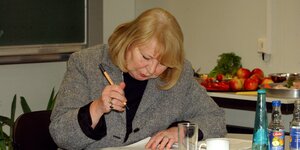 Journalistin Ingrid Kolbe sitzt an einem Schreibtisch mit einem Stift in der Hand und schaut auf einen Text