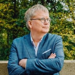 Ein Portraitfoto von Henning Stein, ein Mann mit grauem Haar und Brille in blauer Jacke