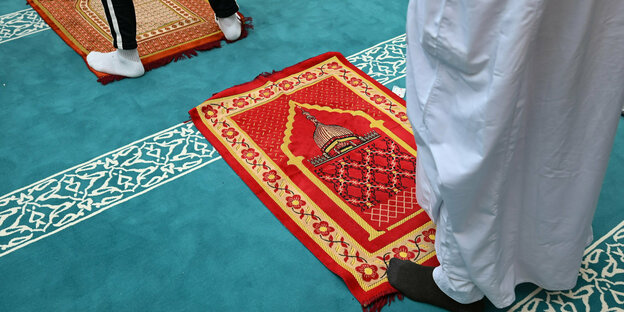 Männer stehen auf Teppichboben auf dem ein kleinerer roter Gebetsteppich liegt