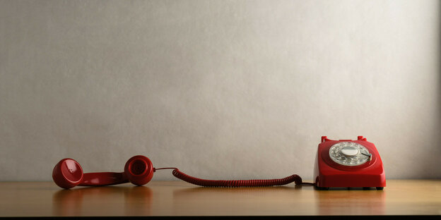 Ein Hörer eines roten Kabel-Telefons liegt neben dem Hörer