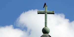 Ein Vogel sitzt auf dem Kreuz einer Kirche.