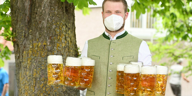 Das Foto zeigt einen Kellner mit Mundschutz und mehreren Biergläsern in einem bayerischen Biergarten.