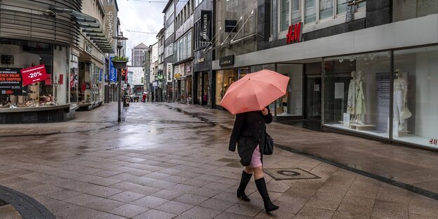Eine einzelne Frau mit einem REgenschirm geht durch eine menschenleere Einkaufsstraße