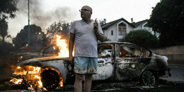 Ein Mann steht vor seinem brennenden Auto.