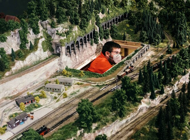 Ein Mann mit Maske schaut durch ein Loch in der Märklin Eisenbahn-Landschaft