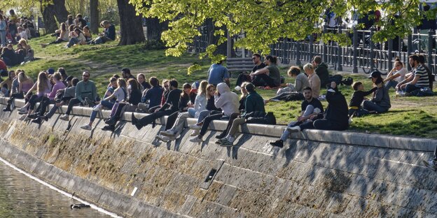 Zahlreiche Menschen sitzen auf einer Ufermauer des Berliner Landwehrkanals