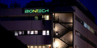 notbeleuchtetes mehrstöckiges Gebäude mit großen Fenstern und grünen Biontech-Leuchtschriftzug auf dem Dach