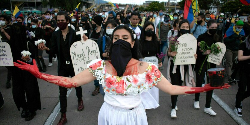 Eine Demonstrantin in einem weißen Kleid und mit roter Farbe beschmierten Händen und Oberkörper läuft am Anfang eines Demonstrationszuges