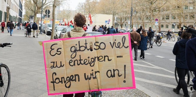 Mann auf einer Straße, der auf dem Rücken ein Transparent trägt. Darauf steht: Es gibt viel zu enteignen - fangen wir an!