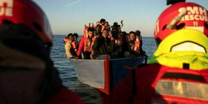 Geflüchtete auf einem Holzboot winken Rettungskräften zu