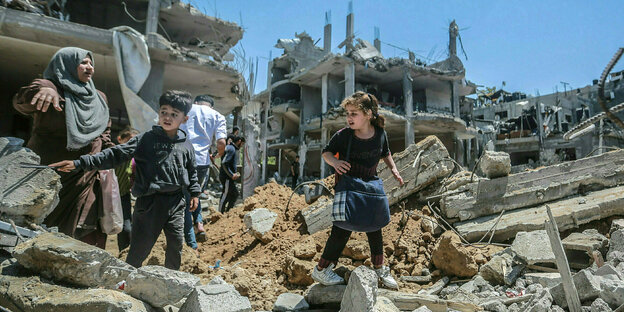 Eine Frau und zwei Kinder gehen durch Trümmerhaufen von zerstörten Gebäuden