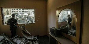 Ein Mann steht in einem zerstörten Zimmer und blickt durch ein Fenster auf Trümmer