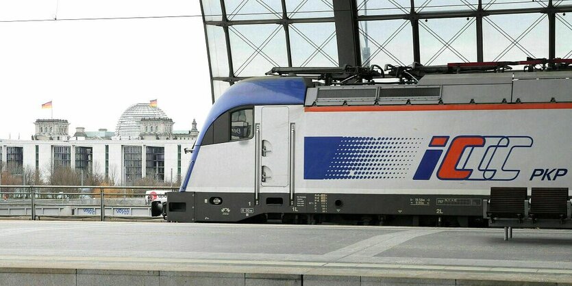 Ein Zug fährt los am Berliner Hauptbahnhof, im Hintergrund sieht man den Deutschen Bundestag