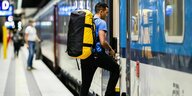Ein Mann steigt mit einem großen Rucksack in einen blau-weißen Zug