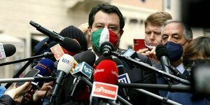 Matteo Salvini umringt von Mikrofonen trägt eine Maske mit der Fahne Italiens und gibt der Presse Auskunft