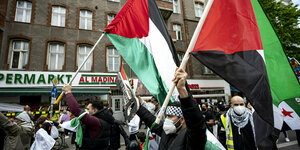 Teilnehmer der Demonstration verschiedener palästinensischer Gruppen laufen mit Palästina-Flaggen durch Neukölln.