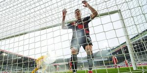 Ein Fußballstürmer steht im Tor und greift ans Tornetz