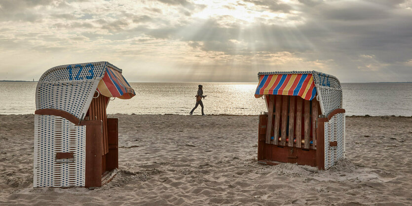 Eine Frau joggt am Strand entlang. Im Vordergrund sind zwei Strandkörbe zu sehen