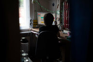 Eine Jugendliche sitzt in einem abgedunkelten Zimmer vor ihrem PC beim Homeschooling.