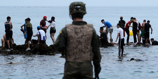 Ein Soldat steht vor jungen Menschen, die im Wasser und auf Felsen stehen
