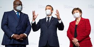 Drei Menschen mit Maske, darunter Frankreichs Präsident Macron