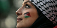 Eine Frau hat eine palästinensiche Flagge auf ihre Wange gemalt