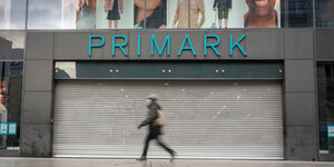 Eine Passantin läuft an einem geschlossenen Modegeschäft mit der Aufschrift "Primark" vorbei.