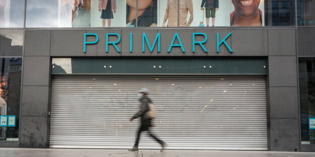 Eine Passantin läuft an einem geschlossenen Modegeschäft mit der Aufschrift "Primark" vorbei.
