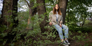 Seher Cemen, eine junge Frau aus Berlin, sitzt in einem Park auf einem Baumstamm