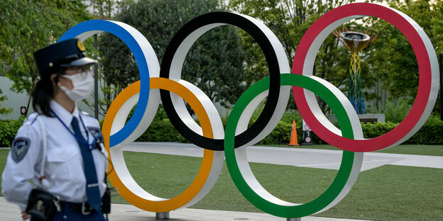 Eine Polizistin steht vor einem Emblem der Olympischen Ringe