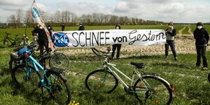 Fahrräder auf einer Wiese, dahinter 8 Aktivist:innen mit Demobanner gegen die A14
