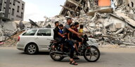 Ein Mann fährt mit 5 Kindern auf seinem Moped an zerstörten Häusern vorbei