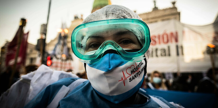 Ärztin in blauem Arztkittel geht hinter eine blaue Wand mit Mundschutz