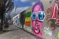 Viele Graffitis auf einer langen Mauer, im Vordergrund ist eine Frau zu sehen mit dem Graffiti "Zero Fucks given"
