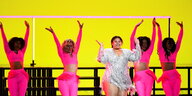 vier Tänzerinnen in rosa Outfit, die Sängerin trägt ein weisses Kostüm