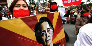 Eine Frau mit roter Maske hält ein Plakat mit einem Porträt von Aung San Suu Kyi