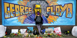 Ein Graffiti von Georg Floyd, davor steht eine Frau, zu ihren Füßen stehen Blumen