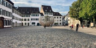 Holzkonstruktion vor alten Häusern, im Innern ist ein Baul sichtbar, auf dem Platz sind Leute