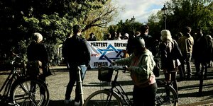 Menschen stehen auf einer Brücke und schauen sich ein Transparent an: Protect Defend Jewish Life