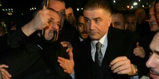 Sedat Peker, in Anzug und mit zurückgegelten Haaren, wird unter einem Regenschirm durch eine Menschenmenge geleitet